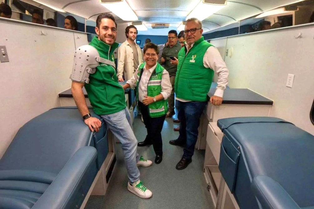 Grupo de personas en un vehículo, algunas vistiendo chalecos verdes, sonriendo y posando para la foto.