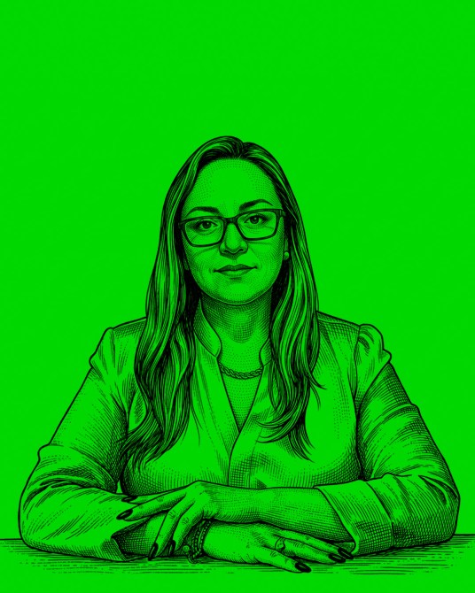 Retrato de una mujer con gafas, cabello largo y oscuro, en un fondo verde brillante, con las manos apoyadas sobre la mesa.