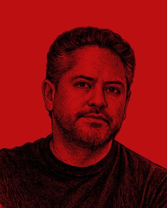 Retrato de un hombre con cabello corto y barba, frente a un fondo rojo.