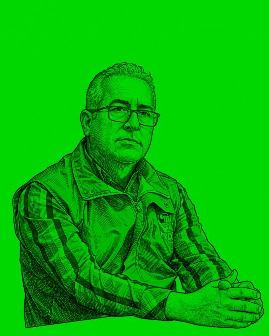 Retrato de un hombre con gafas y chaqueta sobre un fondo verde brillante, sentado con las manos entrelazadas.