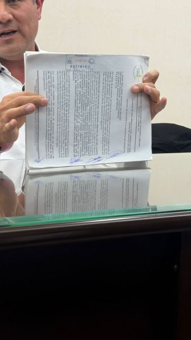 A person holding a document with text and signatures, reflecting on a glass surface.