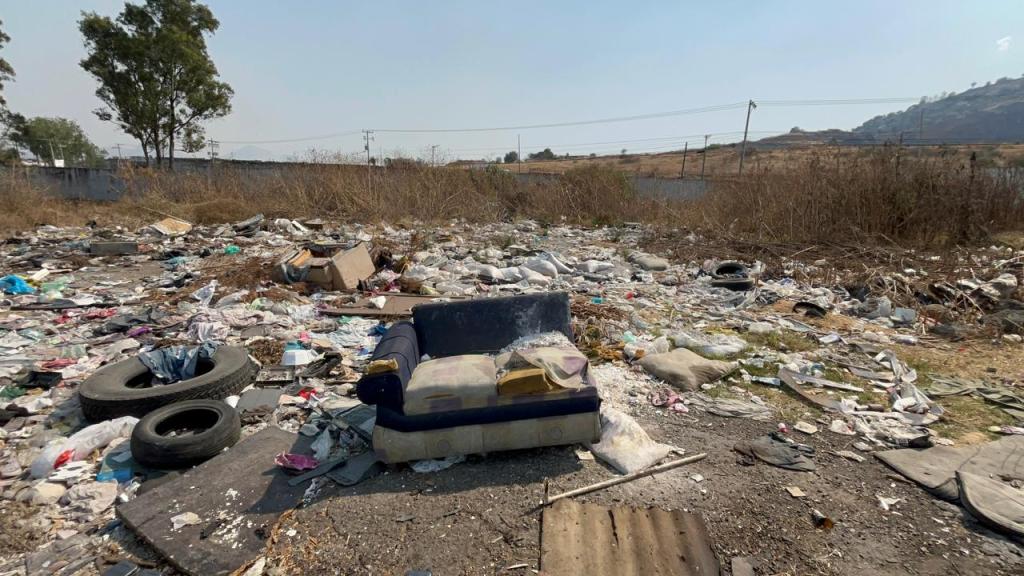 Un área abandonada llena de basura y desechos, con un sofá dañado en el centro y neumáticos viejos alrededor.