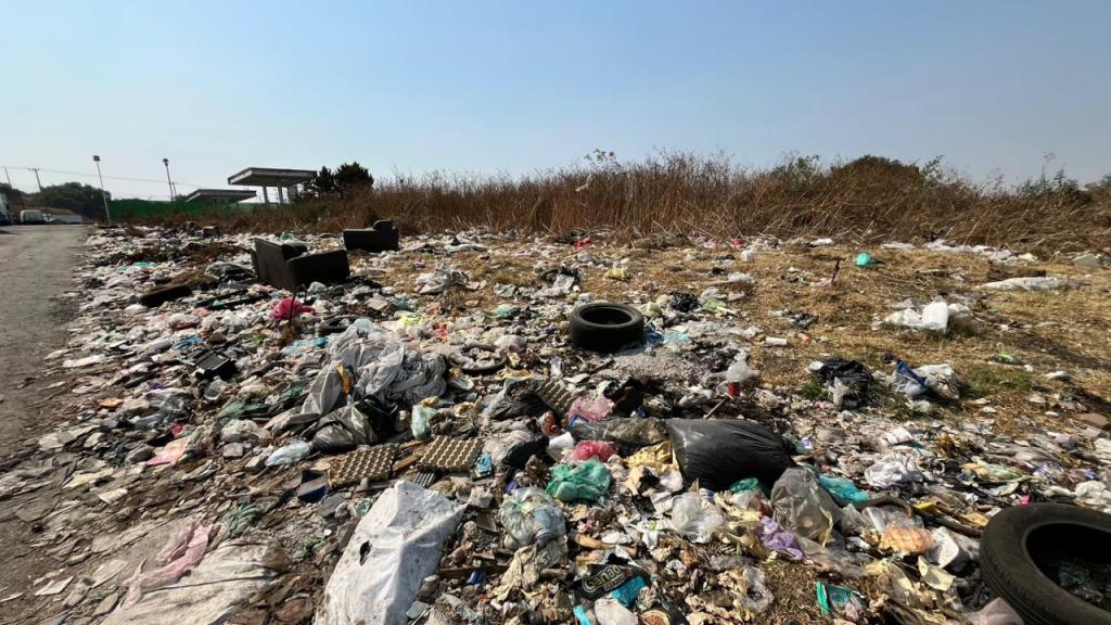 Montón de basura acumulada en un área desierta, con objetos como llantas y muebles viejos mezclados entre desechos plásticos.