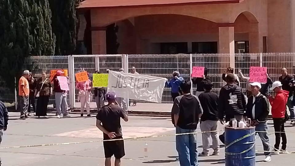 Grupo de personas protestando frente a un edificio, sosteniendo carteles coloridos con mensajes.