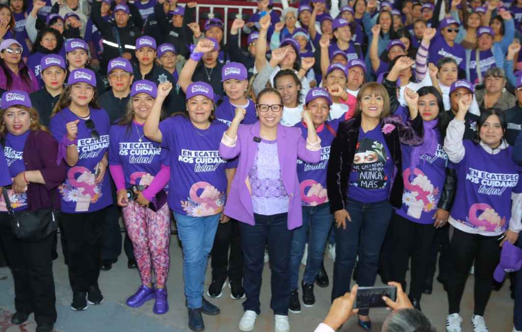 Grupo de mujeres en un evento de apoyo, vistiendo camisetas moradas y levantando los puños en señal de unidad y empoderamiento.