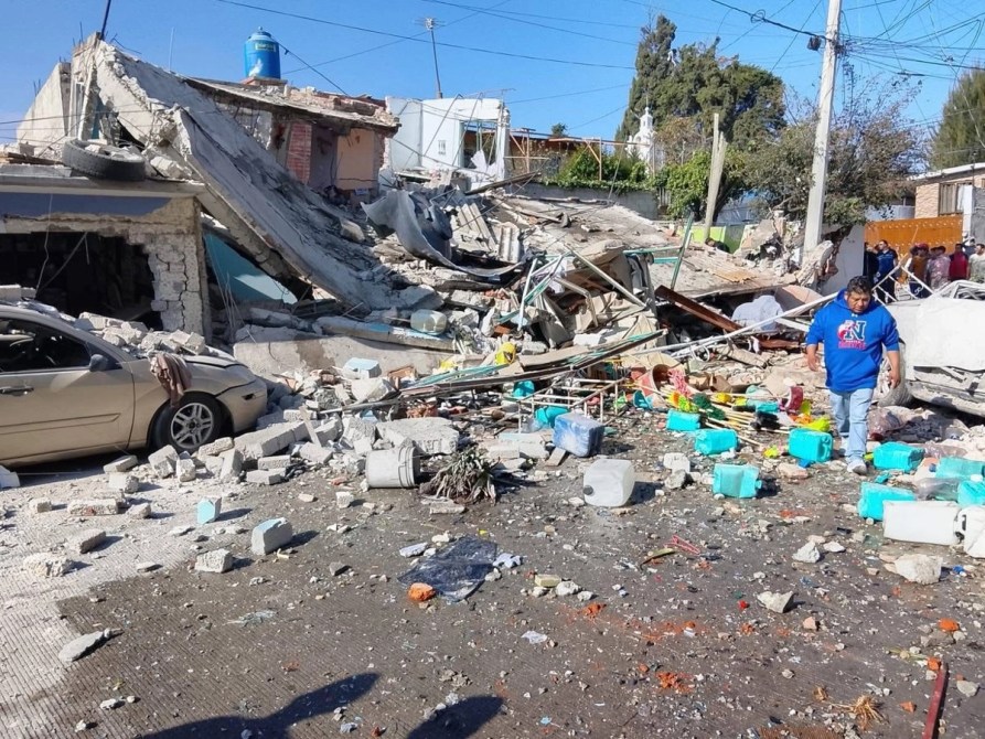 Zona devastada por un terremoto, con escombros de edificios colapsados, un auto dañado y una persona caminando entre los restos.