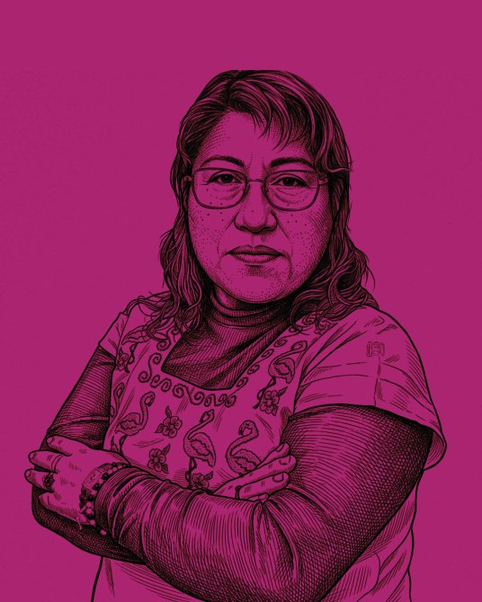 Retrato de una mujer con un suéter oscuro y una blusa con bordados, de pie con brazos cruzados, sobre un fondo morado.