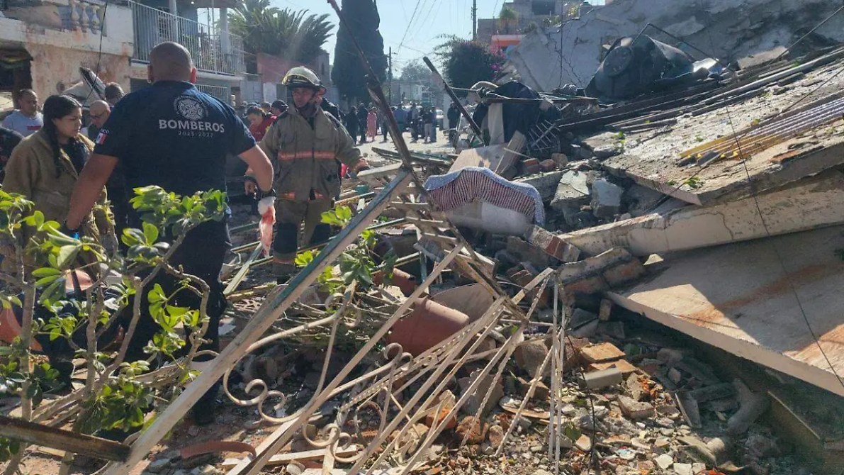 Escena de un derrumbe con rescatistas y bomberos trabajando entre escombros, con personas observando en el fondo.