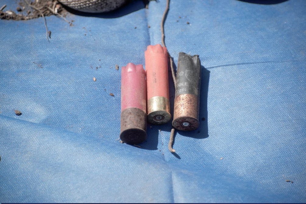 Tres cartuchos de escopeta de diferentes colores sobre una superficie de tela azul.