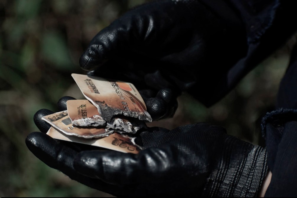 Una mano con guantes negros sostiene tarjetas de crédito quemadas y desgastadas.