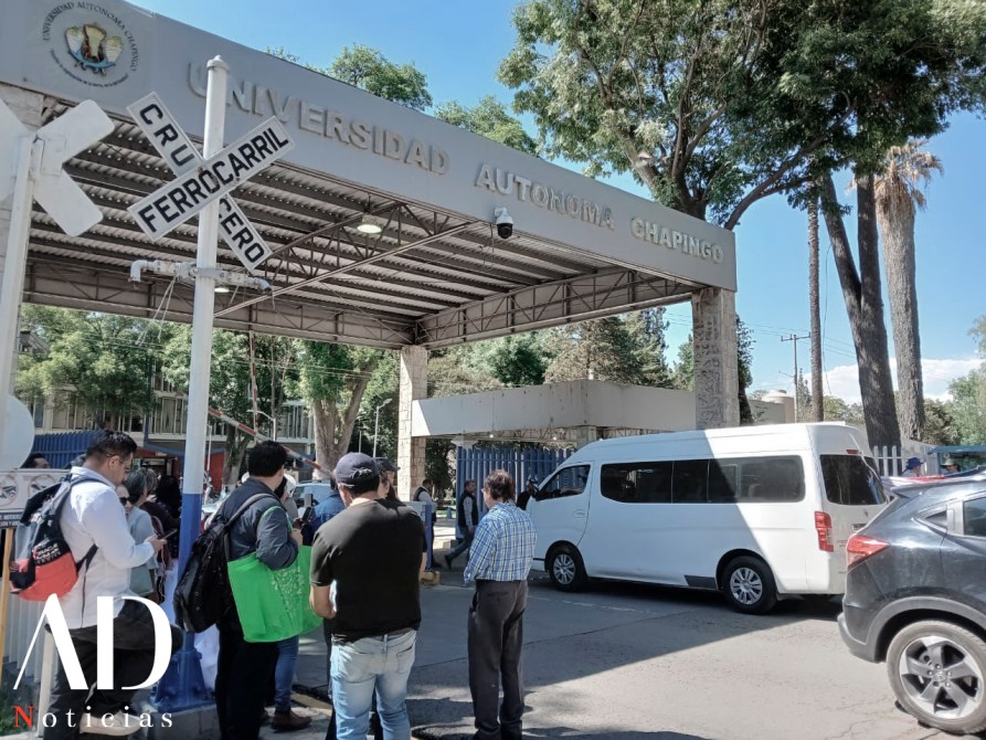 Entrada a la Universidad Autónoma Chapingo con un grupo de personas esperando y un vehículo blanco estacionado.