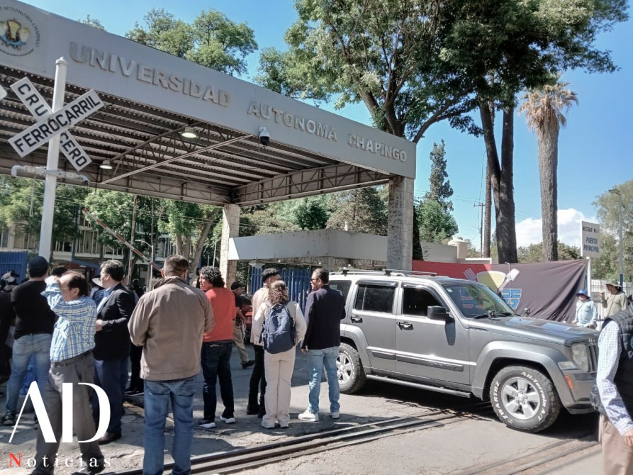 Entrada de la Universidad Autónoma Chapingo con un grupo de personas reunidas y un vehículo estacionado.