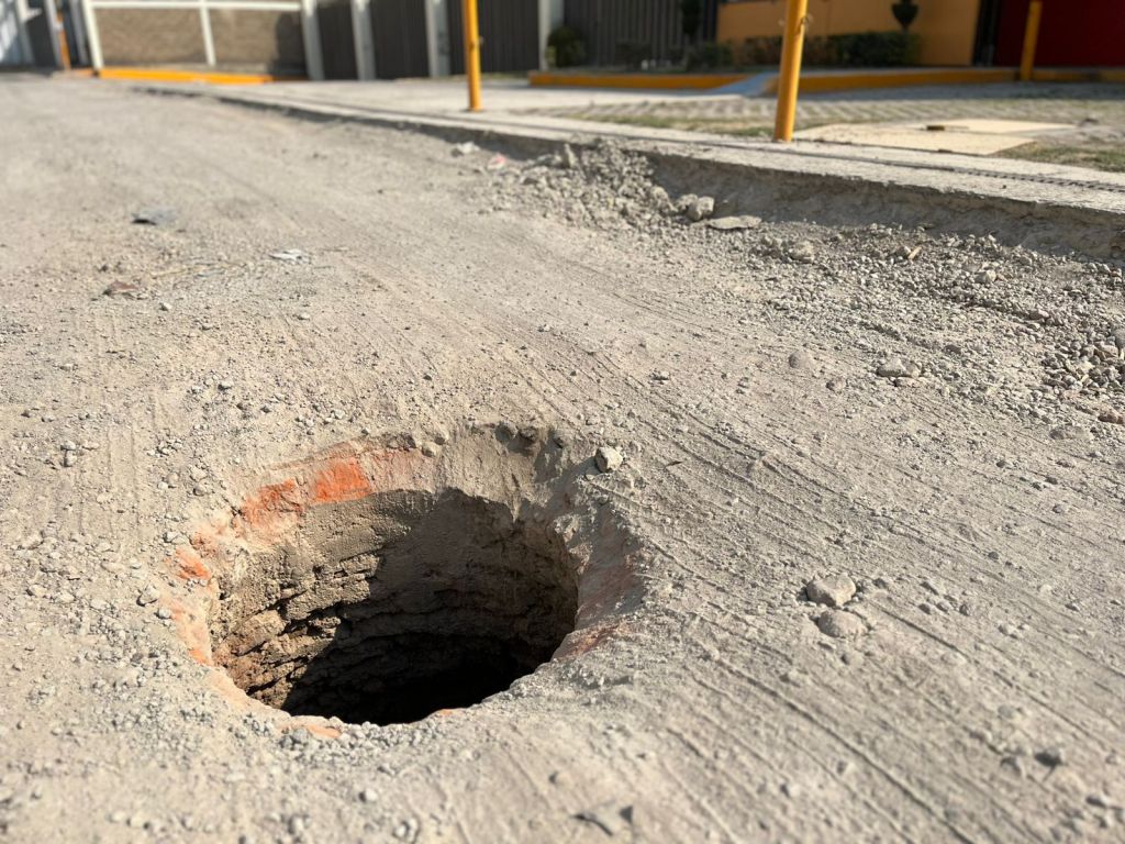 Un agujero profundo en una calle de tierra, rodeado de grava y tierra suelta.