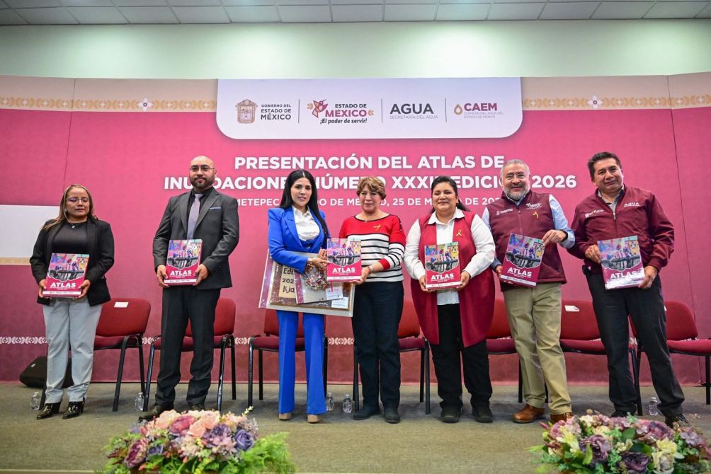 Group of people standing in front of a pink banner with text in Spanish, holding a publication titled 'Atlas' during a presentation event.