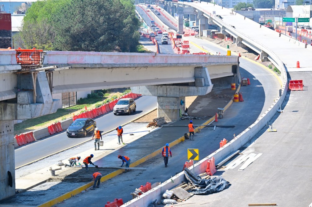 Trabajadores de la construcción realizando labores en una carretera en obras, con vehículos en movimiento y señalización de tráfico.