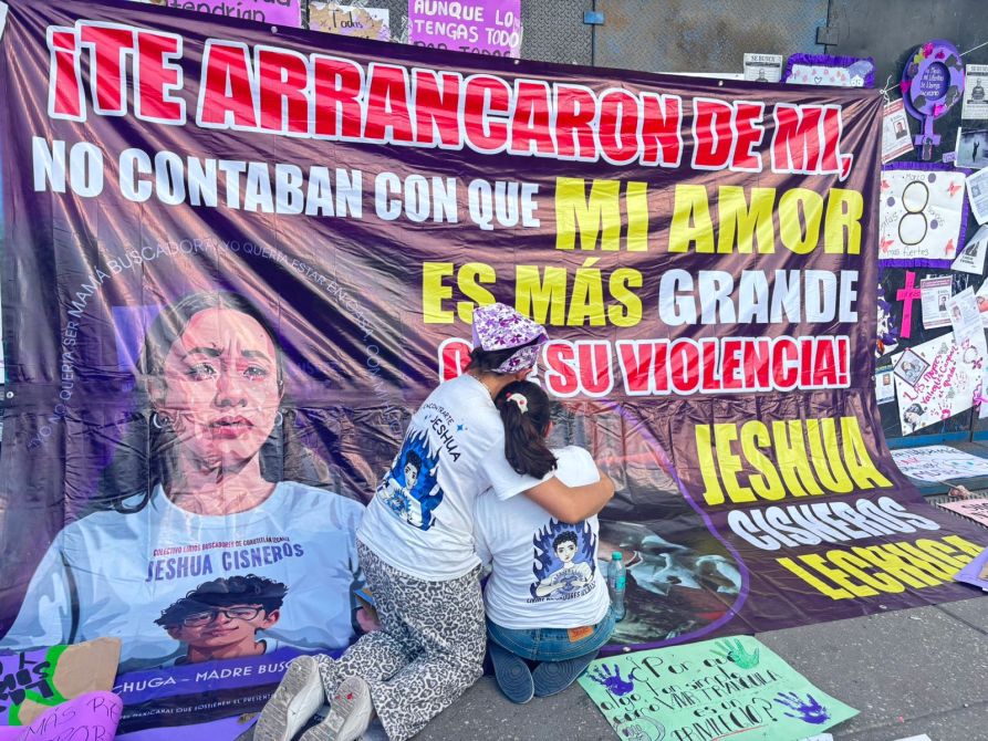 Manifestación con un banner que dice 'Te arrancaron de mí, no contaban con que mi amor es más grande que su violencia', en homenaje a Jeshua Cisneros. Dos personas abrazadas frente al banner.