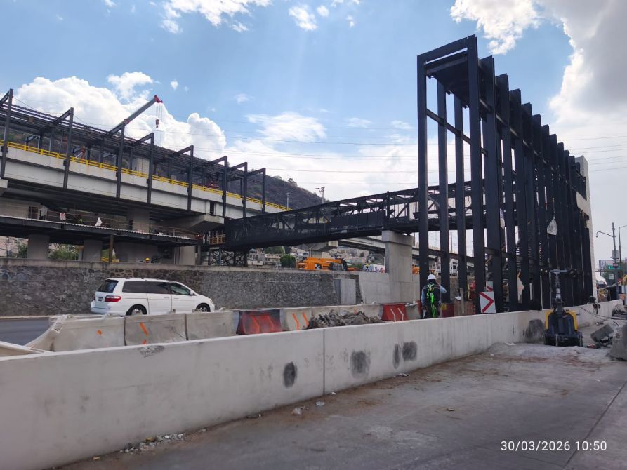Construcción de una estructura metálica sobre una carretera, con vehículos y trabajadores en el sitio.