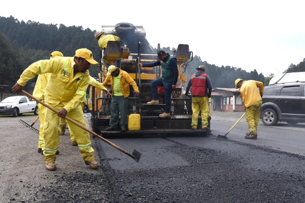 Road construction crew wearing yellow reflective clothing working on asphalt paving.