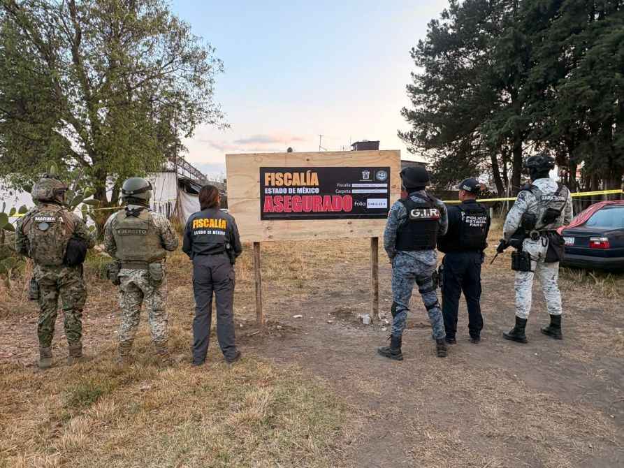 Tres agentes de seguridad, uno con uniformes de la Marina y el Ejército, observan un letrero de la Fiscalía en una escena asegurada, con un auto de fondo y árboles alrededor.
