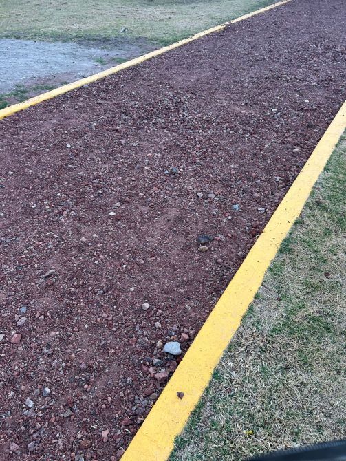 A gravel pathway bordered by a bright yellow line, surrounded by grassy areas.