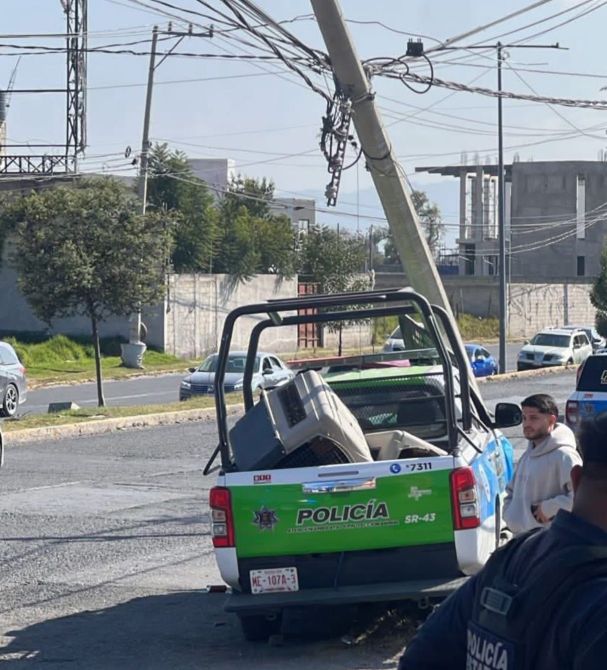 Una camioneta de policía con un mueble en la parte trasera, un poste de luz inclinado y cables eléctricos cruzando la calle.