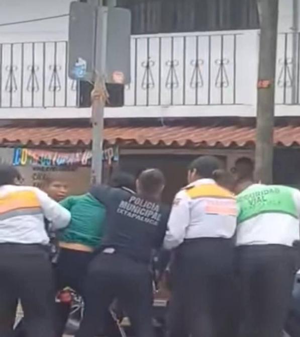 Agentes de policía arrestando a un hombre en una calle mientras un grupo de personas observa.