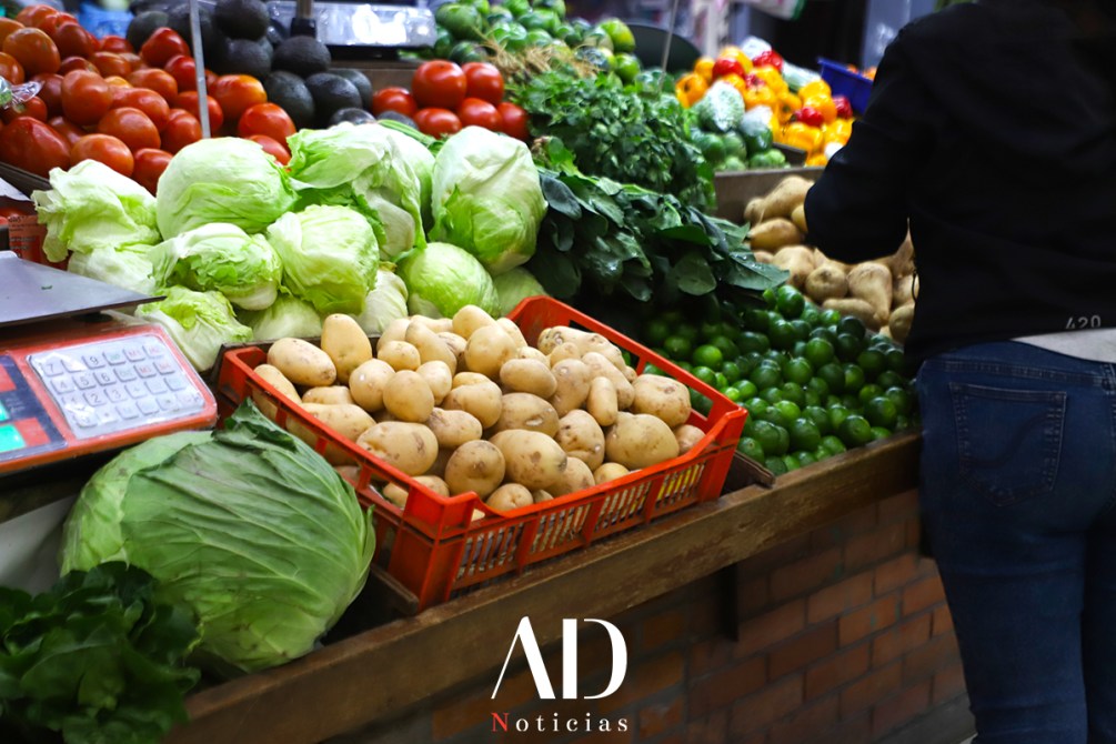 Mesa de mercado con diferentes vegetales, incluyendo lechugas, papas, limones y una variedad de frutas y verduras coloridas.