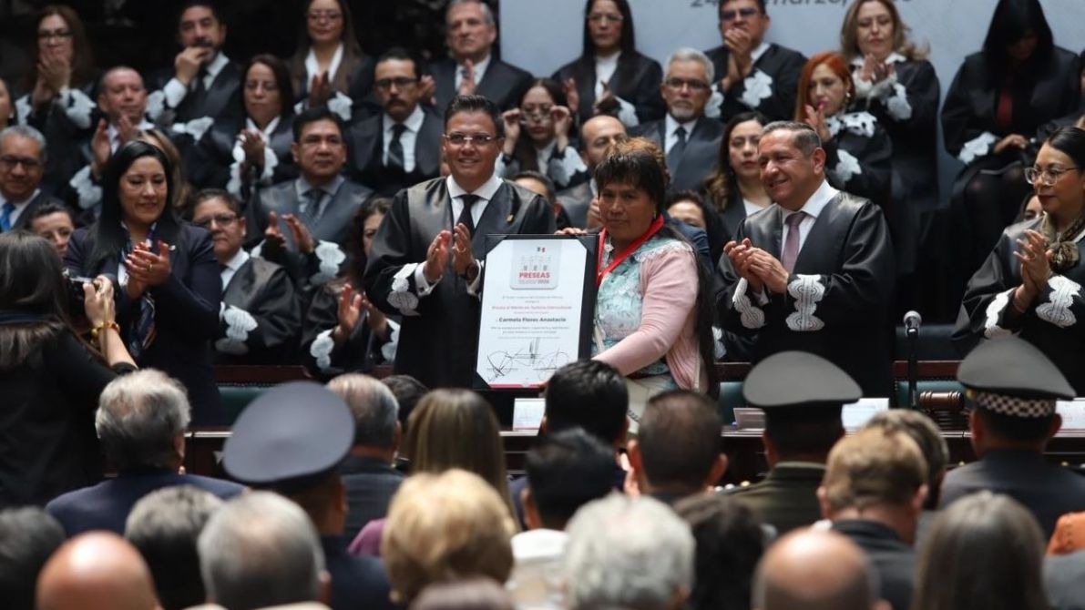 Ceremonia de entrega de un reconocimiento a Carmen Rosa Andrade, con varios asistentes aplaudiendo en el fondo.