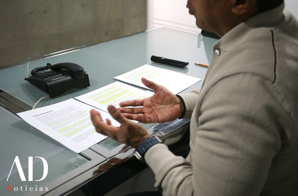 A person gesturing with their hands while discussing documents on a glass table, with a telephone and a pen visible in the background.