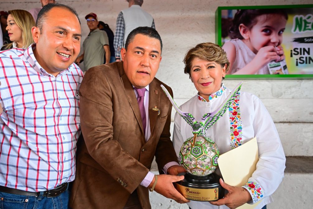Three individuals pose together, one holding a decorative trophy shaped like a ball with an eagle design, while smiles and a certificate are present in the image.