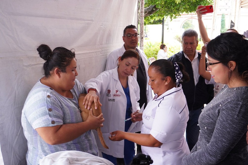 Una mujer sostiene un perro mientras es atendida por profesionales de la salud en un evento comunitario, rodeada de varias personas observando.