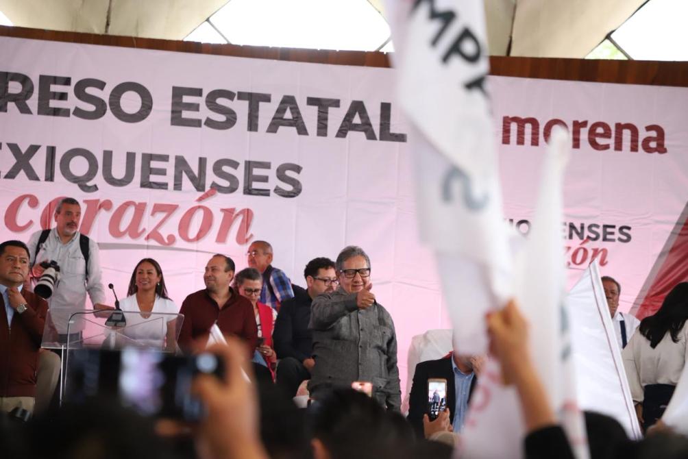 Evento político de Morena con varias personas en un escenario, ondeando banderas y con un fondo donde se lee 'Congreso Estatal Texiquenses' y 'Corazón'.