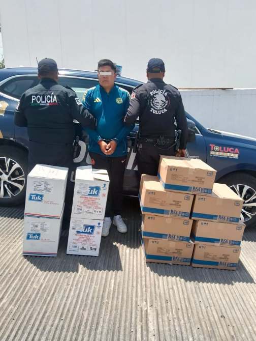 Un hombre detenido por la policía de Toluca, junto a cajas de productos, en un área de estacionamiento.