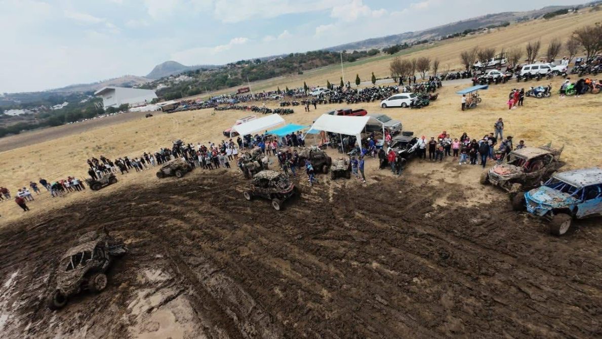 Vista aerial de un evento de coches todoterreno en un terreno de barro, con una multitud de espectadores y varias carpas, rodeados de vehículos y motocicletas.
