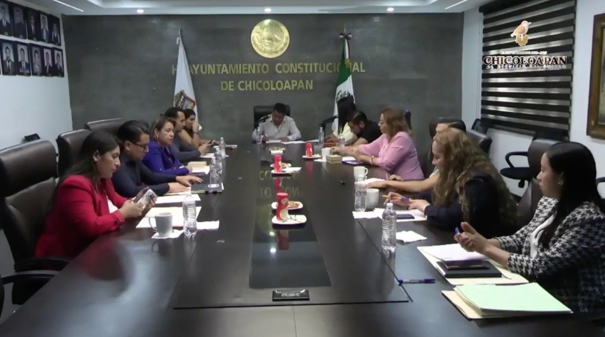 Reunión en el Ayuntamiento de Chicoloapan, con varios participantes sentados alrededor de una mesa larga, discutiendo y tomando notas.