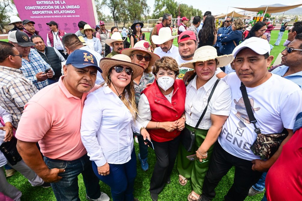 A group of people posing for a photo at an outdoor event, with some wearing hats and sunglasses. A banner in the background announces the inauguration of a sports unit in Atlalongo.