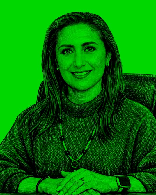 Retrato de una mujer sonriente con cabello largo, usando un suéter y un collar, sentada frente a un fondo verde brillante.