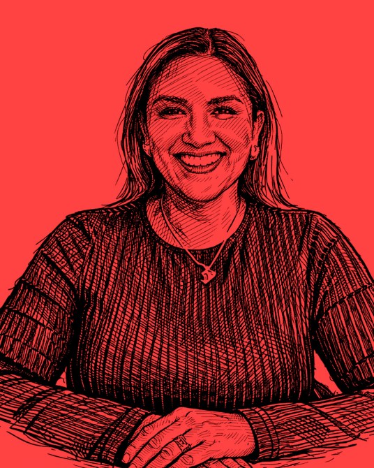 Retrato de una mujer sonriente con cabello largo, vestida con un suéter oscuro, sobre un fondo rojo.