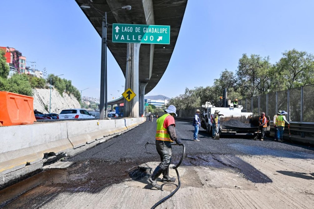 Trabajadores realizando trabajos de pavimentación en una carretera con señalización de dirección hacia Lago de Guadalupe y Vallejo.