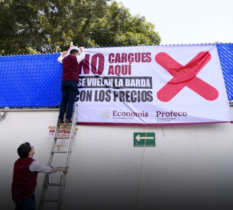 Dos trabajadores colocando un cartel que dice 'NO CARGUES AQUÍ' en una pared, con un símbolo de prohibición y referencias a la Secretaría de Economía y Profeco.