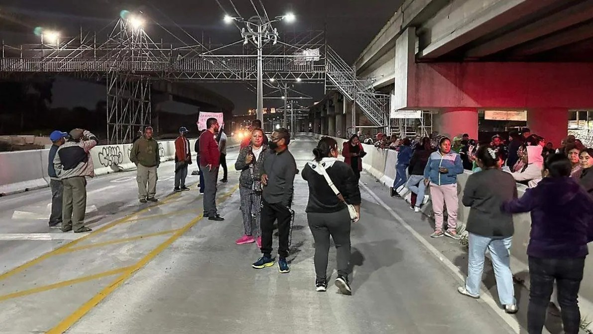 Un grupo de personas en una calle, bajo la luz artificial de la noche, algunas conversando y otras mirando hacia el frente.
