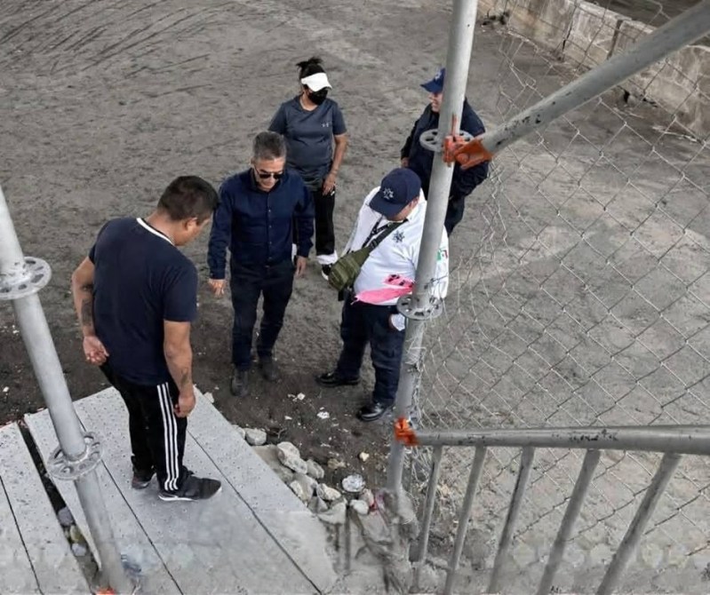 Un grupo de personas observando un área de construcción con suelo de tierra y escombros.
