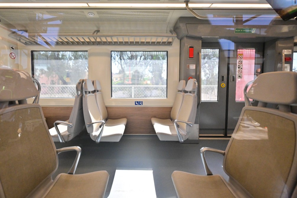 Interior de un tren mostrando asientos vacíos y ventanas amplias.