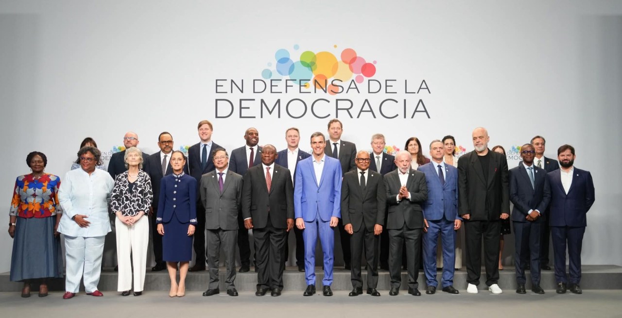 A group photograph of diverse political leaders and representatives standing in front of a backdrop that reads 'EN DEFENSA DE LA DEMOCRACIA.'