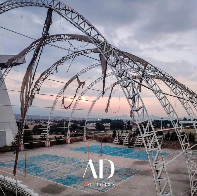 Estructura de acero parcialmente destruidas con telas colgantes en un espacio vacío al atardecer.