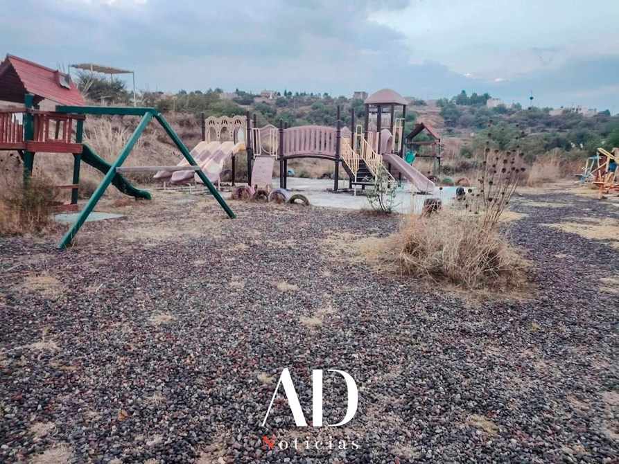 Parque infantil abandonado con juegos en un entorno seco y con vegetación escasa.