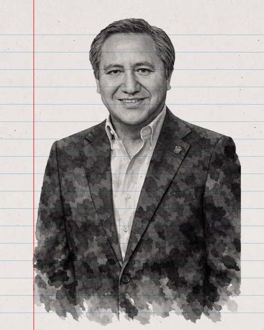 Retrato de un hombre sonriendo, vestido con un blazer oscuro y una camisa blanca, sobre un fondo con líneas de cuaderno.