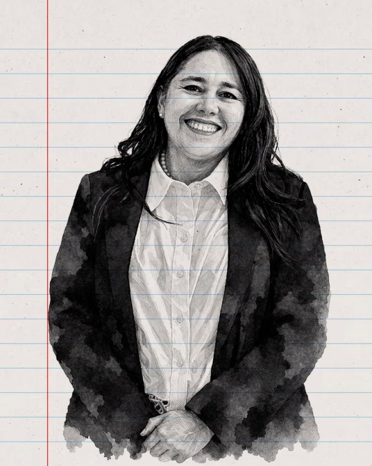 Retrato de una mujer sonriendo, vestida con un blazer negro y una camisa blanca, frente a un fondo de papel de cuaderno rayado.