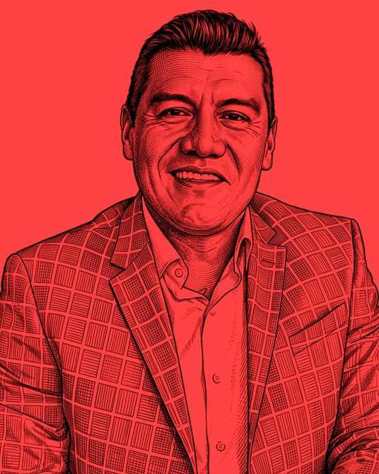 Retrato de un hombre sonriente con un saco a cuadros sobre un fondo rojo.