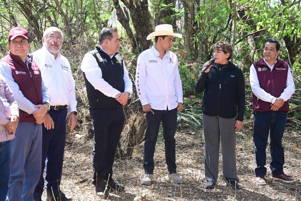 Seis personas de pie en un área boscosa, algunas sostienen micrófonos. Una mujer habla mientras los demás escuchan atentamente.